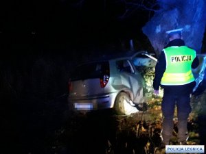 policjant stoi obok samochodu, który wjechał w drzewo