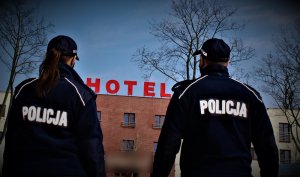policjanci stoją przed budynkiem na którym jest napis hotel