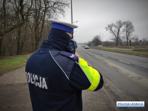 policjant z urządzeniem do pomiaru prędkości stoi na drodze