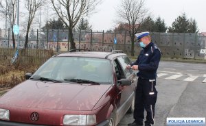 umundurowany policjant stoi przy samochodzie koloru czerwonego na drodze