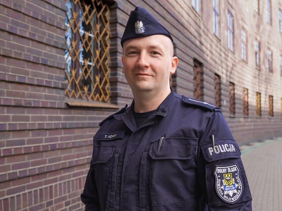 Umundurowany policjant na tle budynku Komendy Wojewódzkiej Policji we Wrocławiu.