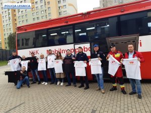 Przy autobusie stoją mężczyźni z różnych służb i trzymają koszulki krwiodawstwa.