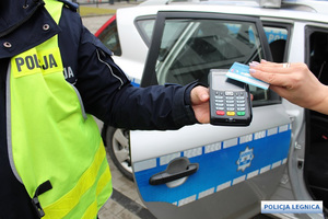 Policjant trzyma terminal płatniczy, do którego kobieta przykłada kartę.