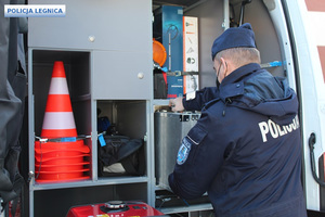 Policjant wyjmuje metalową walizkę umieszczoną pośród specjalistycznego sprzętu do wykonywania czynności na miejscach zdarzeń.