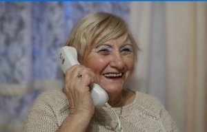 Uśmiechnięta seniorka trzyma słuchawkę telefonu przy uchu.