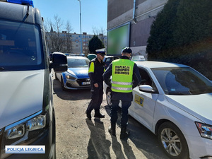 Policjant i funkcjonariusz Inspekcji Transportu Drogowego kontrolują pojazd koloru białego, w tle radiowóz i pojazd ITD.