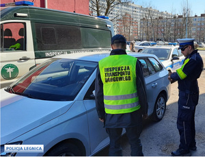 Policjant i funkcjonariusz Inspekcji Transportu Drogowego kontrolują pojazd koloru białego, w tle radiowóz i pojazd ITD.