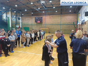 Zastępca Komendanta Miejskiego policji w Legnicy komisarz Kamil Piasecki wręczający medal uczestnikom konkursu