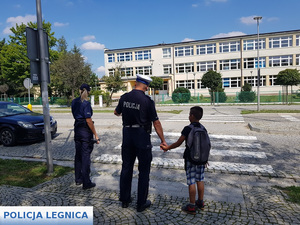 policjant ruchu drogowego pomaga chłopcu przejść przez pasy tłumacząc zasady ruchu drogowego