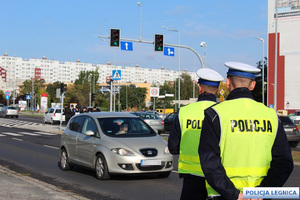 dwóch policjantów ruchu drogowego pełniących nadzór nad ruchu drogowym stojąc przy drodze