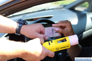 policjant trzymający urządzenie do badania trzeźwości zwrócone w kierunku kierującego, druga ręką odbiera od niego dokument prawa jazdy