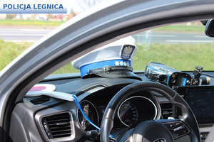 radiowóz oznakowany z otwartymi drzwiami od kierowcy wewnątrz widać na podszybiu czapkę policjanta ruchu drogowego tarcze do zatrzymywania oraz ręczny miernik prędkości