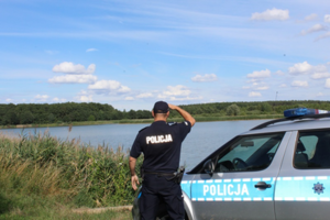 policjant stojący obok radiowozu obserwujący zbiornik wodny