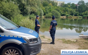 policjantki nad brzegiem stawu kontrolujące bezpieczeństwo nad zbiornikiem wodnym, po lewej stronie stoi oznakowany radiowóz