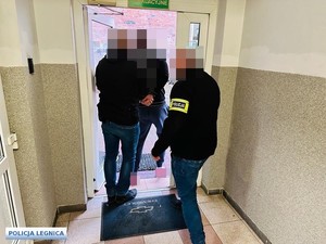 mężczyzna w kajdankach prowadzony przez policjantów