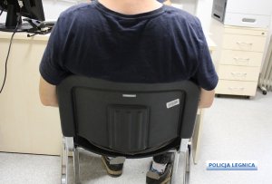 mężczyzna siedzi na krześle przed biurkiem, ubrany w ciemną koszulkę i spodnie  dresowe w tle po prawej stronie szafka z szufladami, na której stoi drukarka