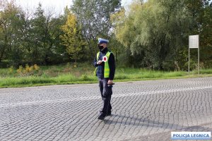 policjant ruchu drogowego stoi na drodze w maseczce i trzyma w ręce tarcze do zatrzymywania pojazdów