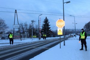policjanci wraz z funkcjonariuszami Służby Ochrony Kolei stoją przy przejeździe kolejowym