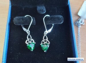 otwarte niebieskie pudełko z ciemnym wypełnieniem a w środku wiszą kolczyki w kolorze srebrnym z kamieniami w kolorze zielonym