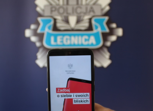 telefon komórkowy trzymany w dłoni, a na nim uruchomiona aplikacja kwarantanna domowa w kolorze biało-czerwonym